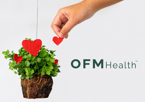 Mano colocando un corazón de papel sobre una planta verde junto al logo de OFM Health